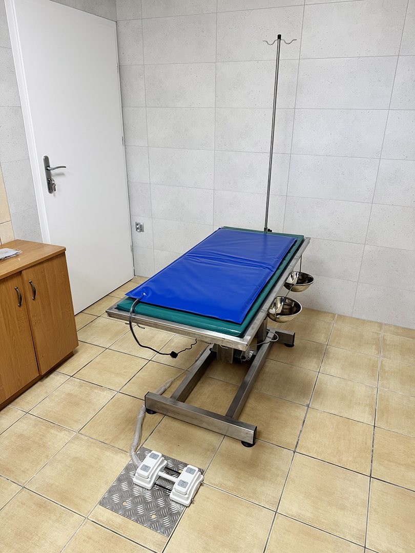 Stół zabiegowy z matą grzewczą i stojakiem na kroplówkę w pomieszczeniu zabiegowym